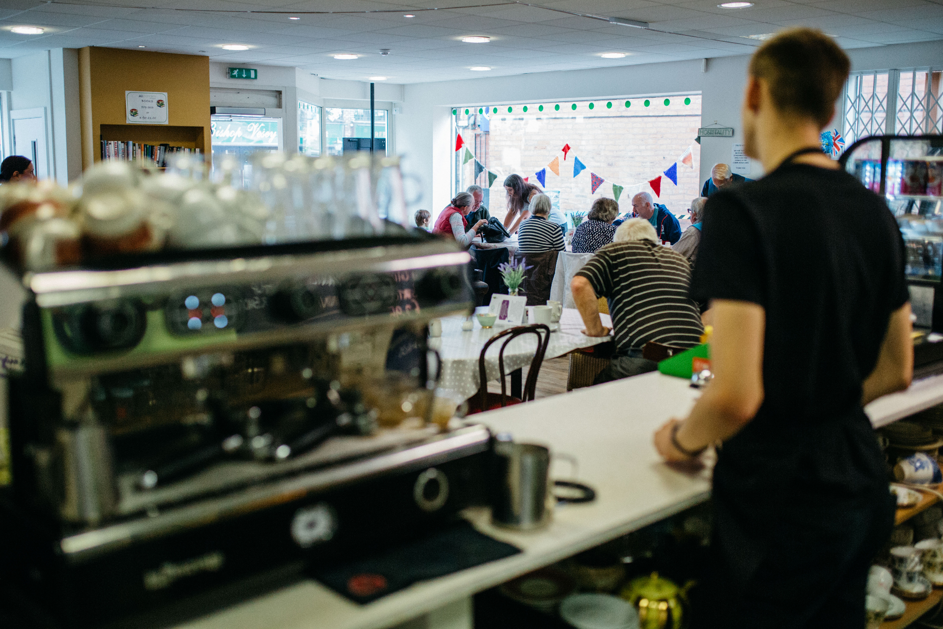 Inside Communitea Café with guests gathered around tables and the coffee machine in the foreground