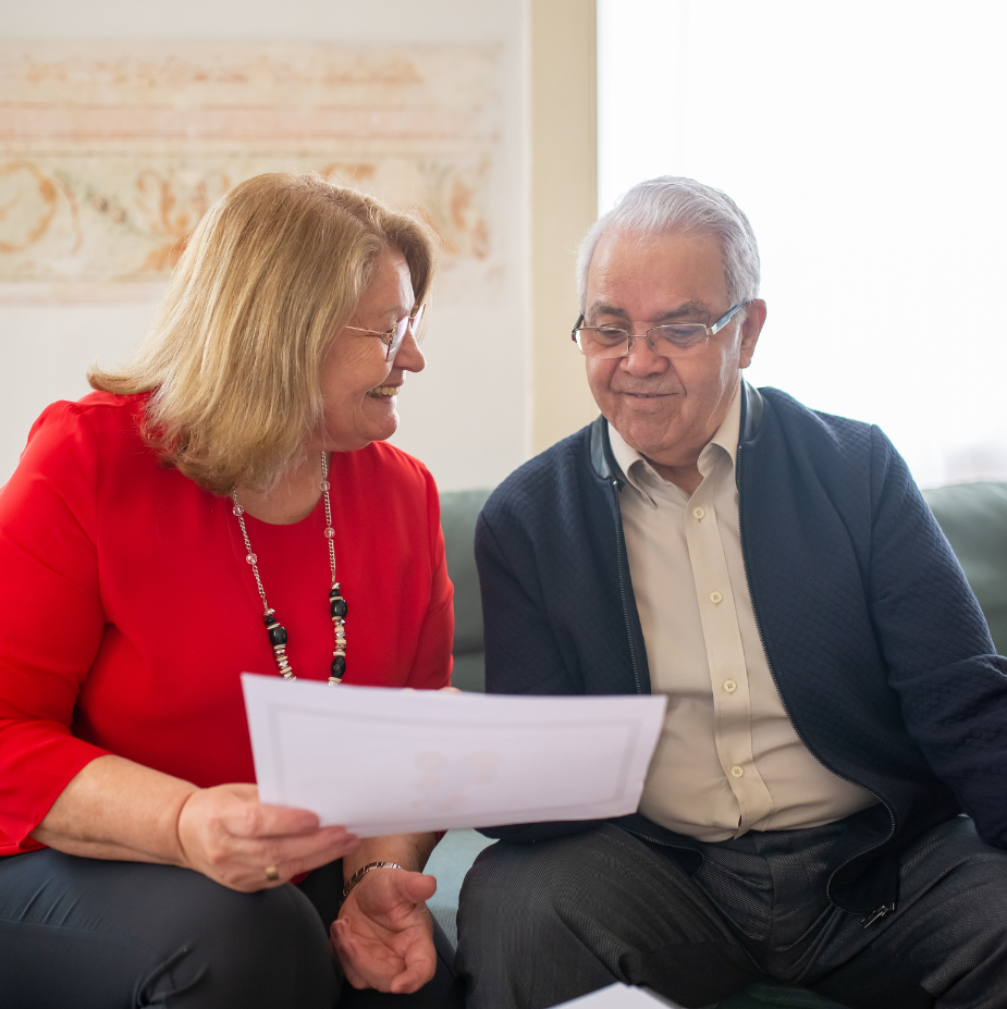 A staff member in a red top reviewing papers with an older gentleman.