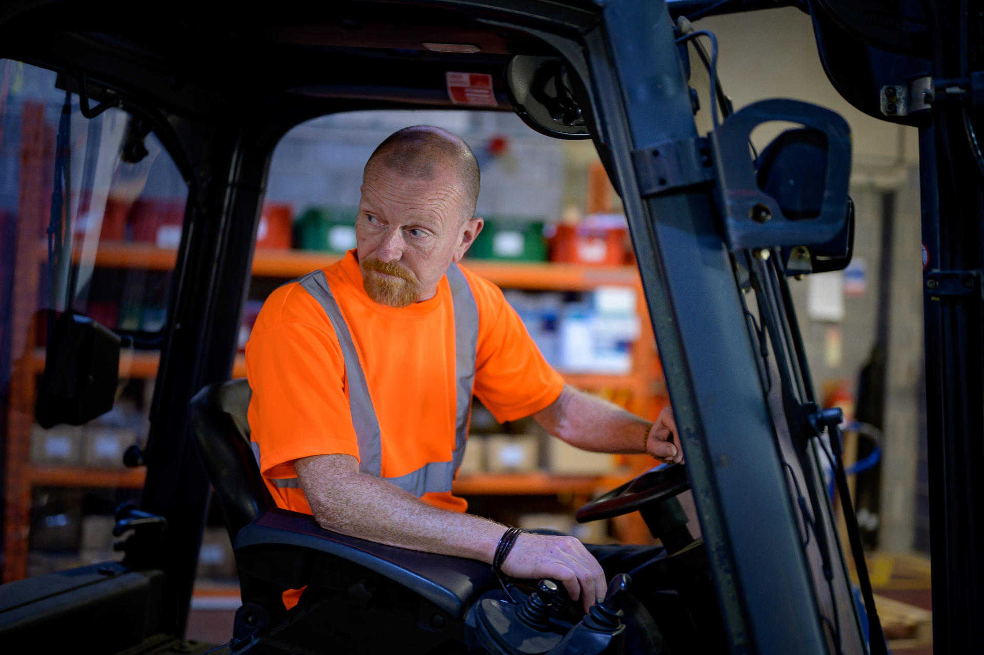 A tradesperson in a hi-vis shirt operating a forklift in a warehouse