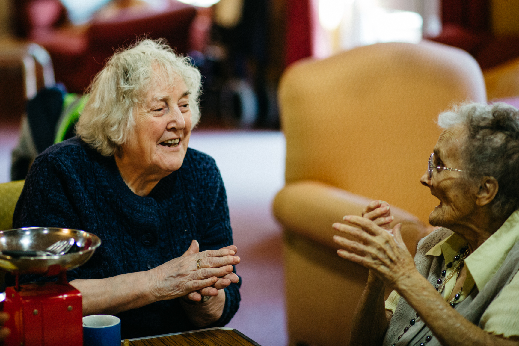 Two older women chatting together in a cosy lounge