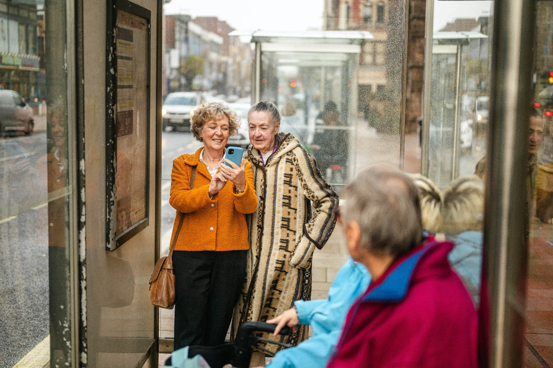 Two older women looking at a phone together at a bus stop